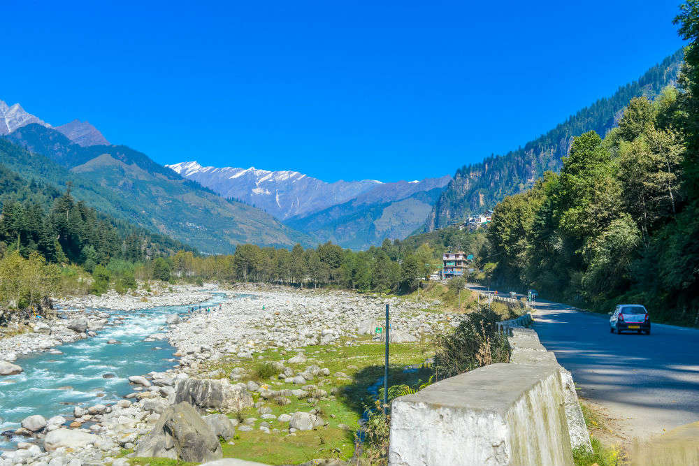 road besides a flowing rivulet with mountains in the backdrop 
Manali-tourism-places